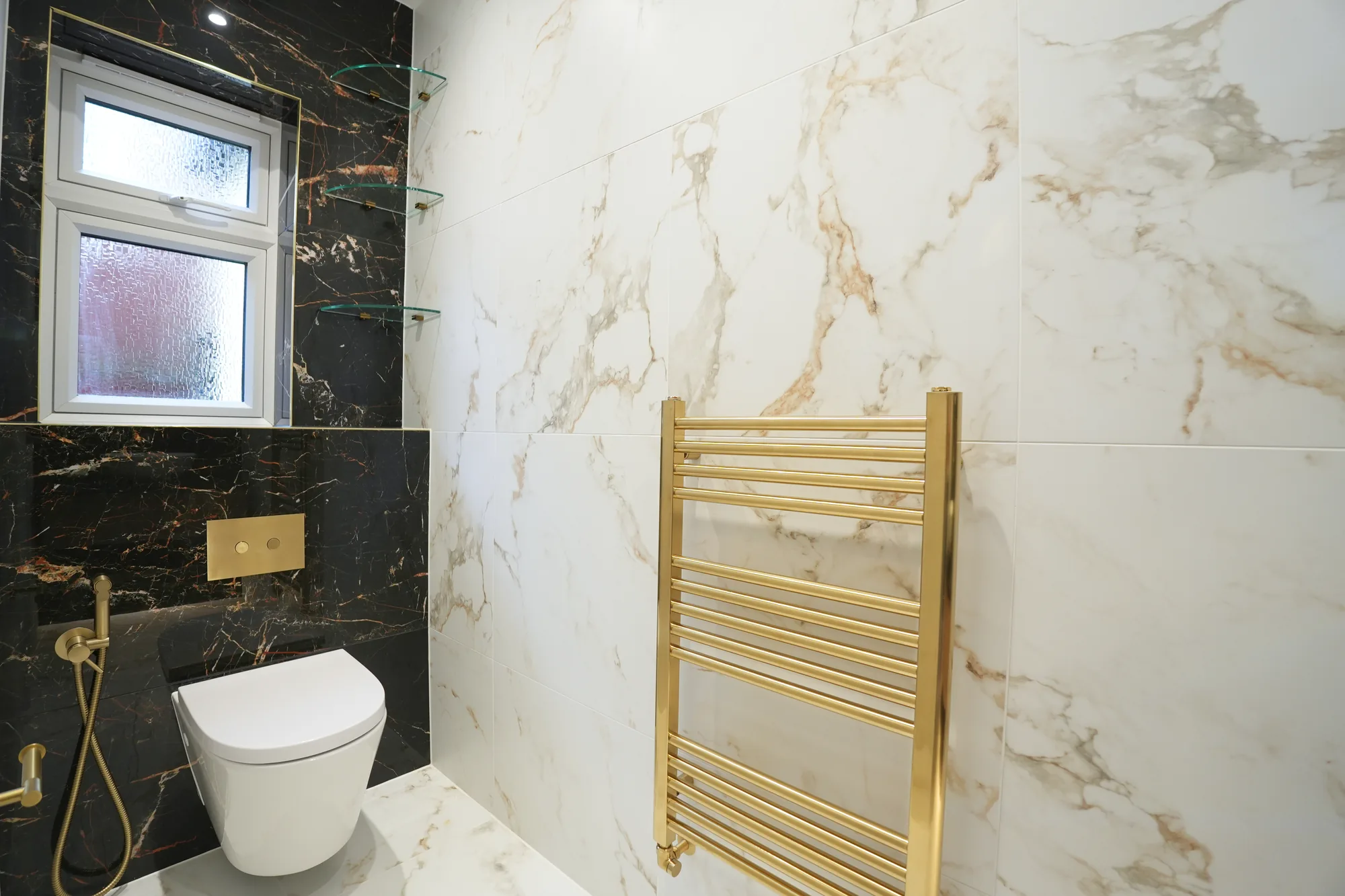 Marble cloakroom with brass fittings and gold towel rail at the Chigwell project.