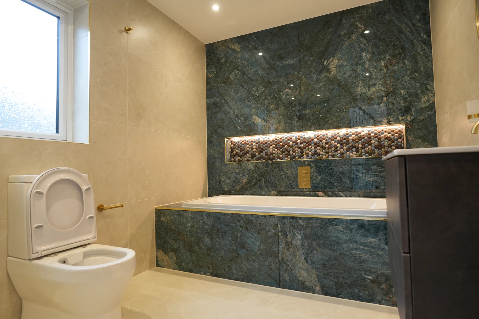 Green marble bathroom with mosaic niche and brass trim at the Chigwell project