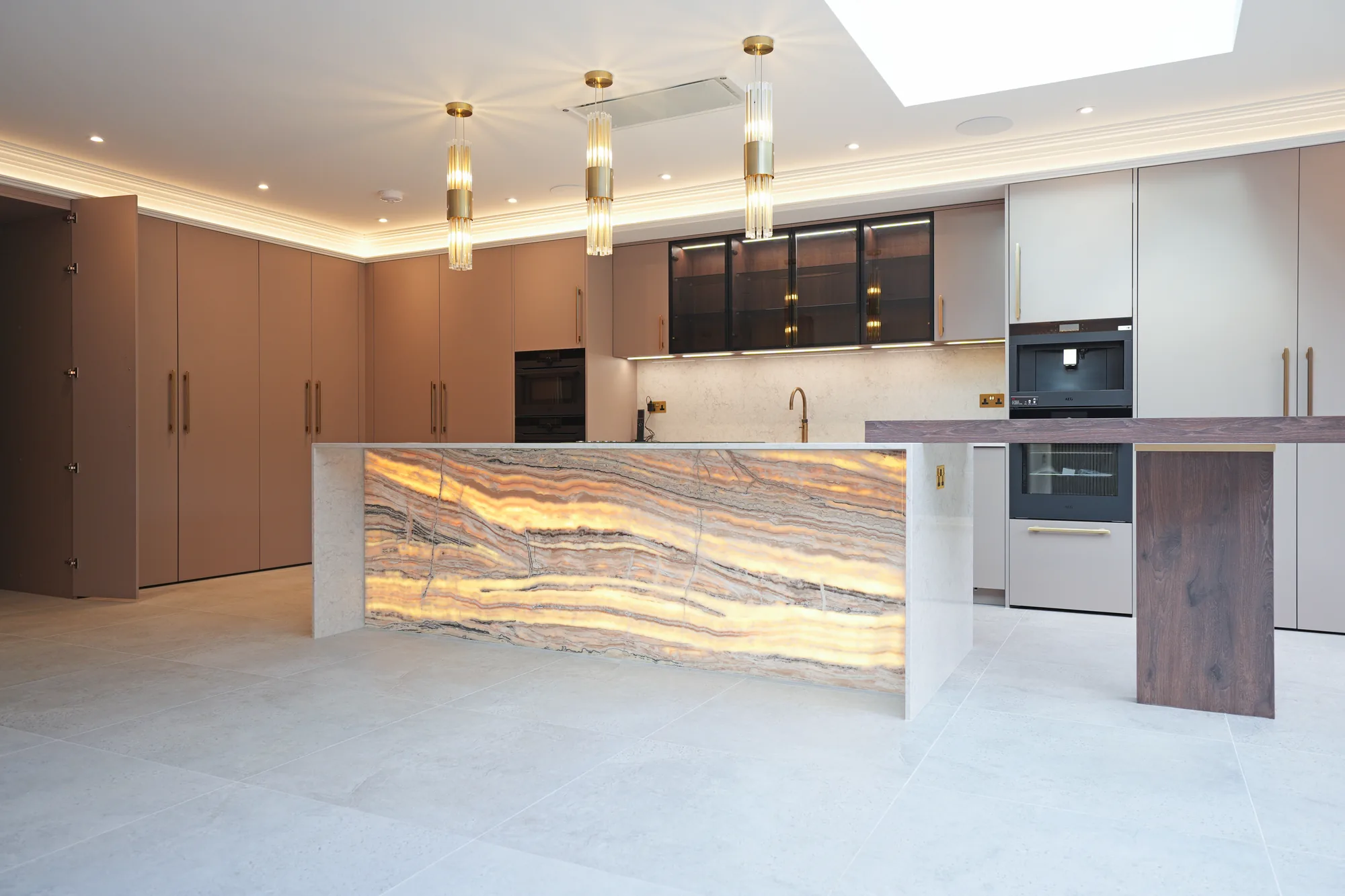 Backlit onyx kitchen island with brass pendant lights at the Chigwell design and build project.