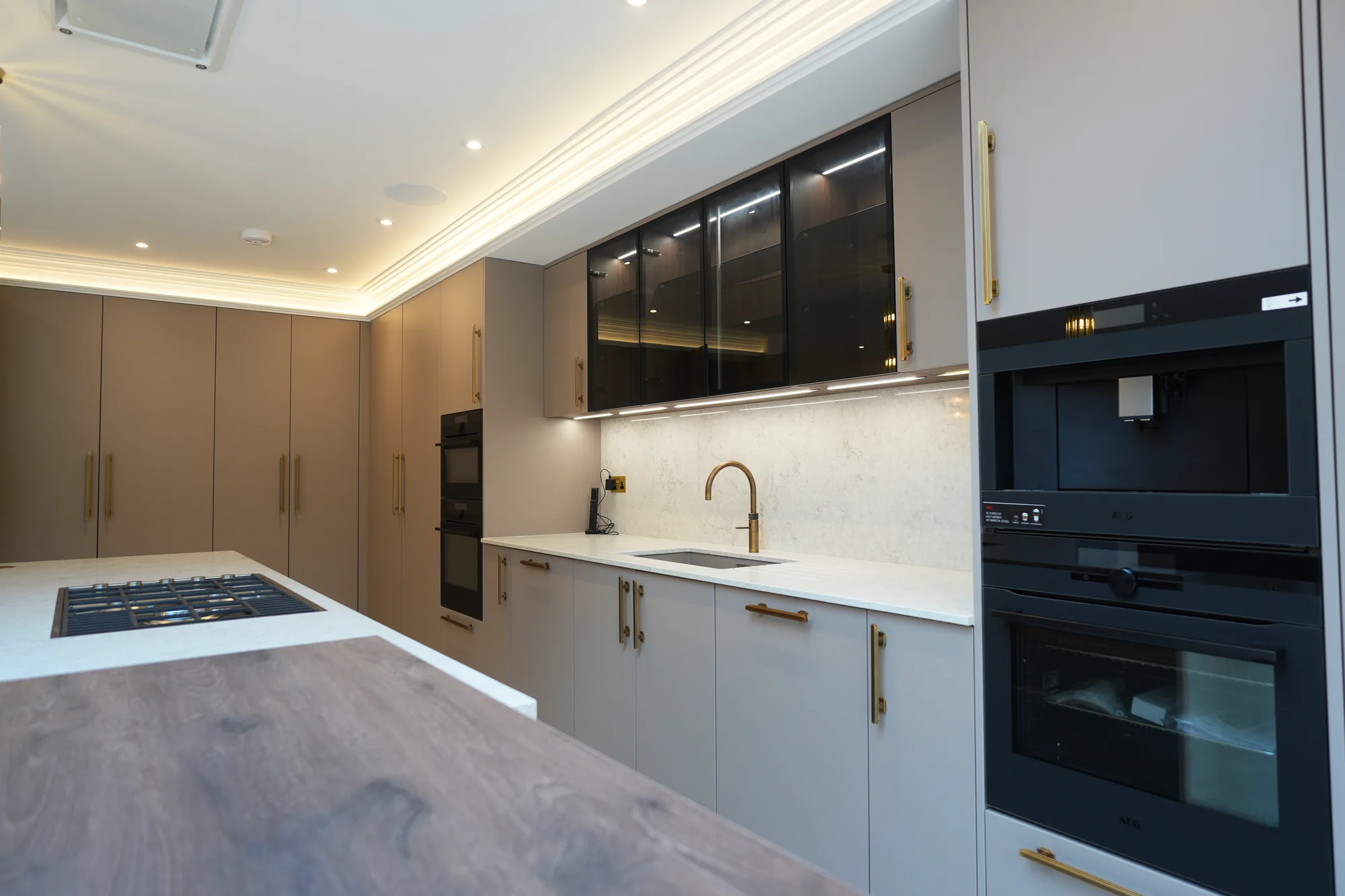 Kitchen run at Chigwell with brass handles, island hob and glazed display cabinets