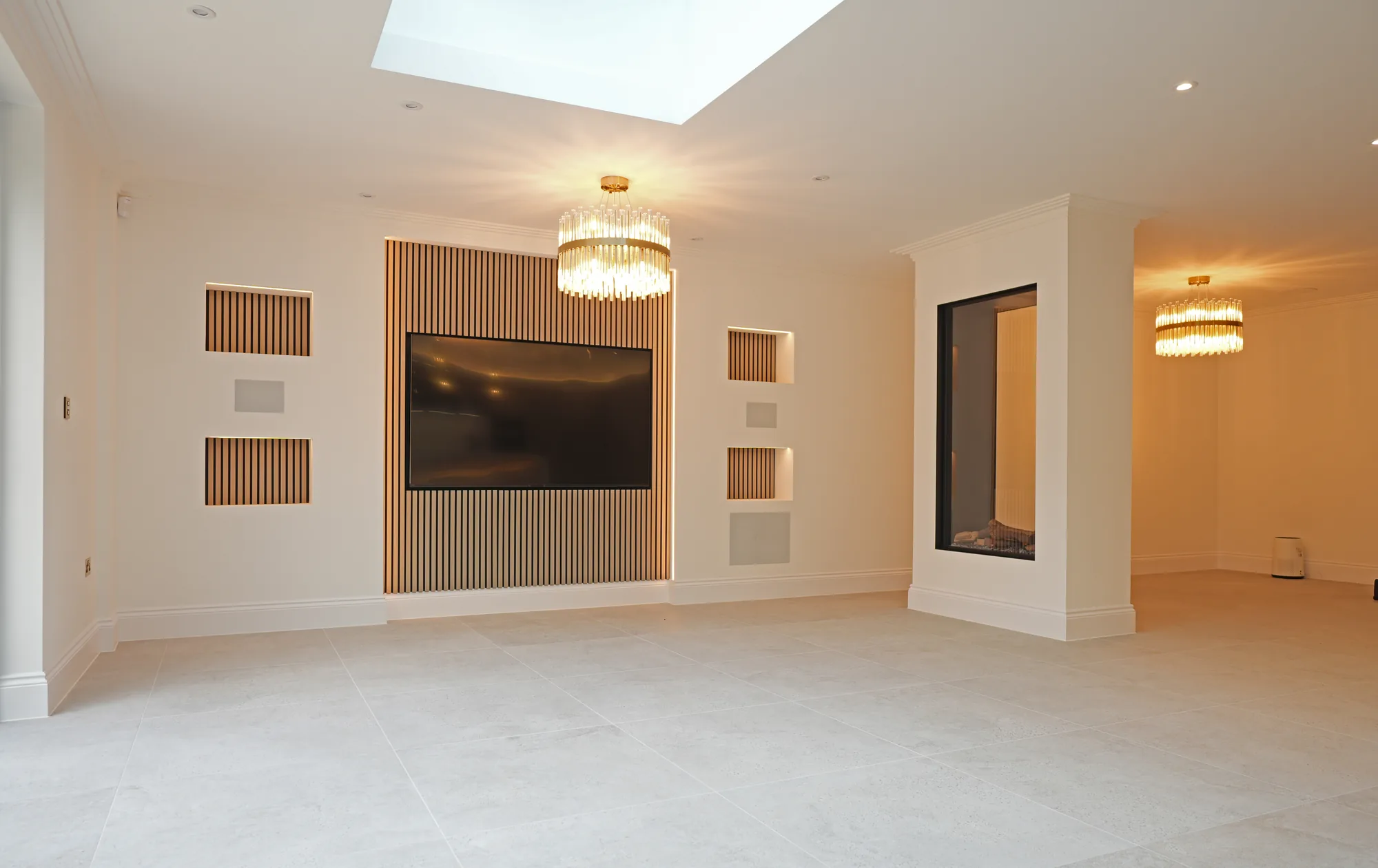 Open plan living space at Chigwell with media wall, slatted panelling and feature chandeliers