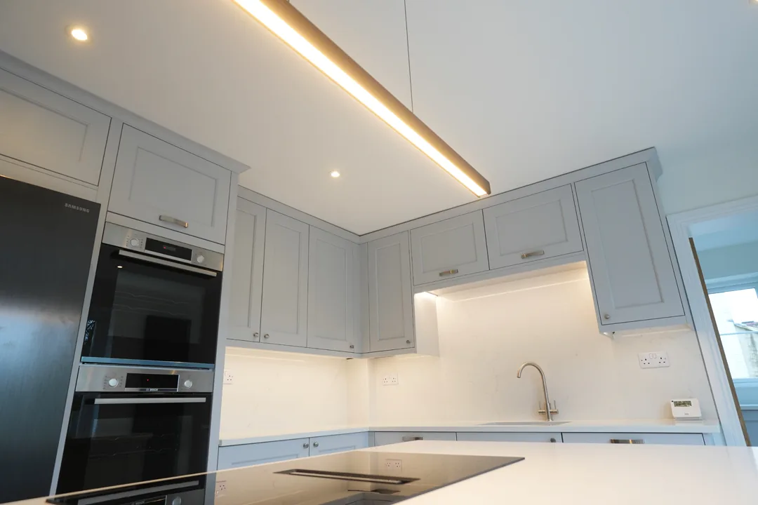 Kitchen run at the Cold Norton house with integrated ovens, stone worktops and pendant lighting.