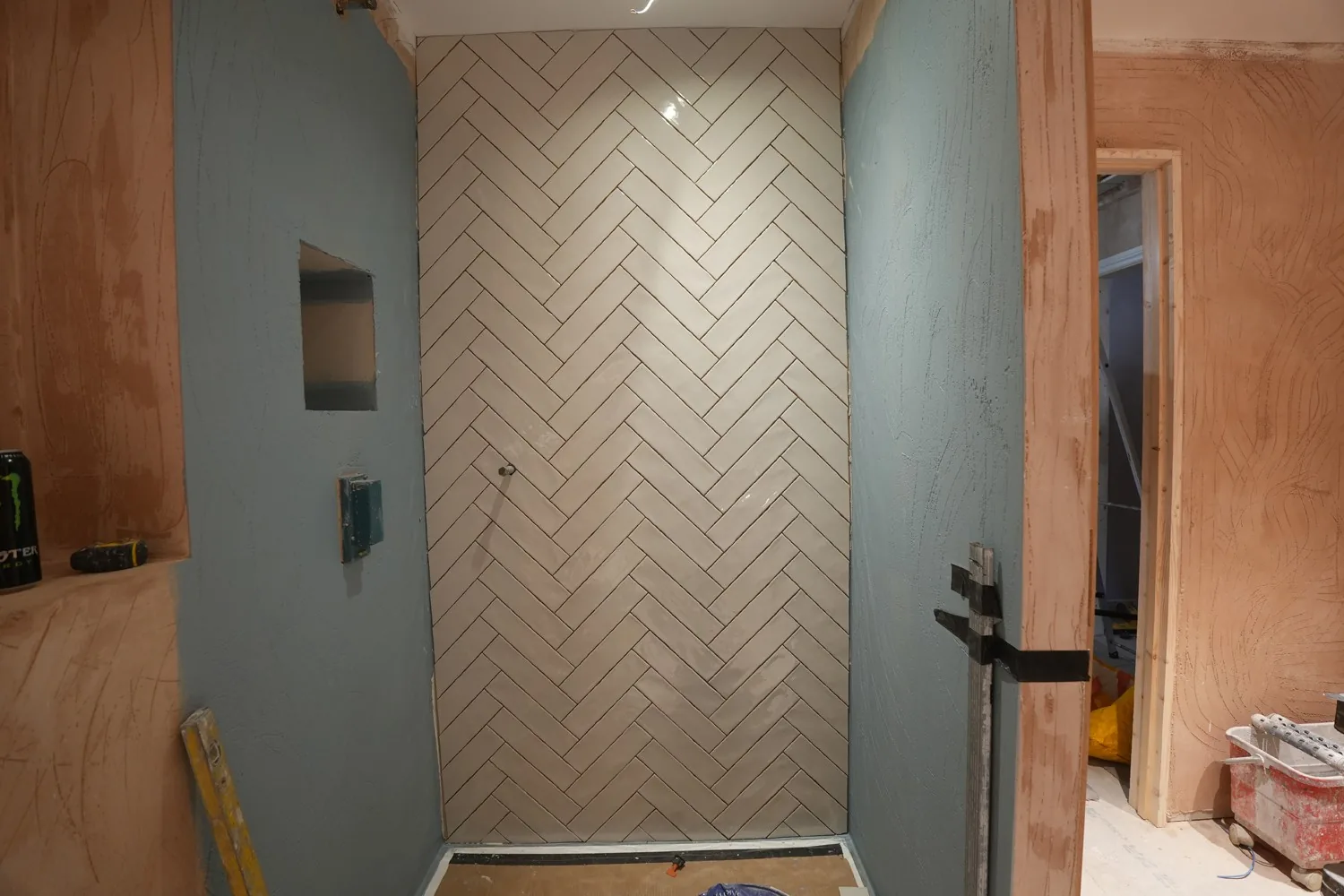 The newly tiled herringbone shower wall at Brentwood, set floor to ceiling between blue painted walls.