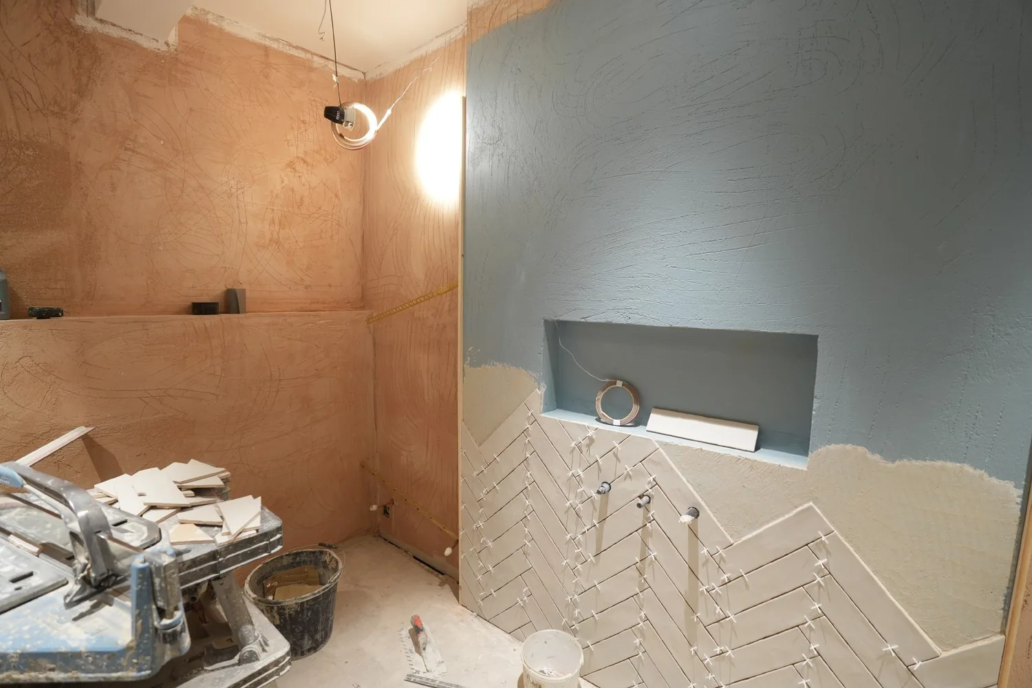 Herringbone wall tiling rising against fresh plaster and painted walls in a Brentwood shower room, spacers still in place.