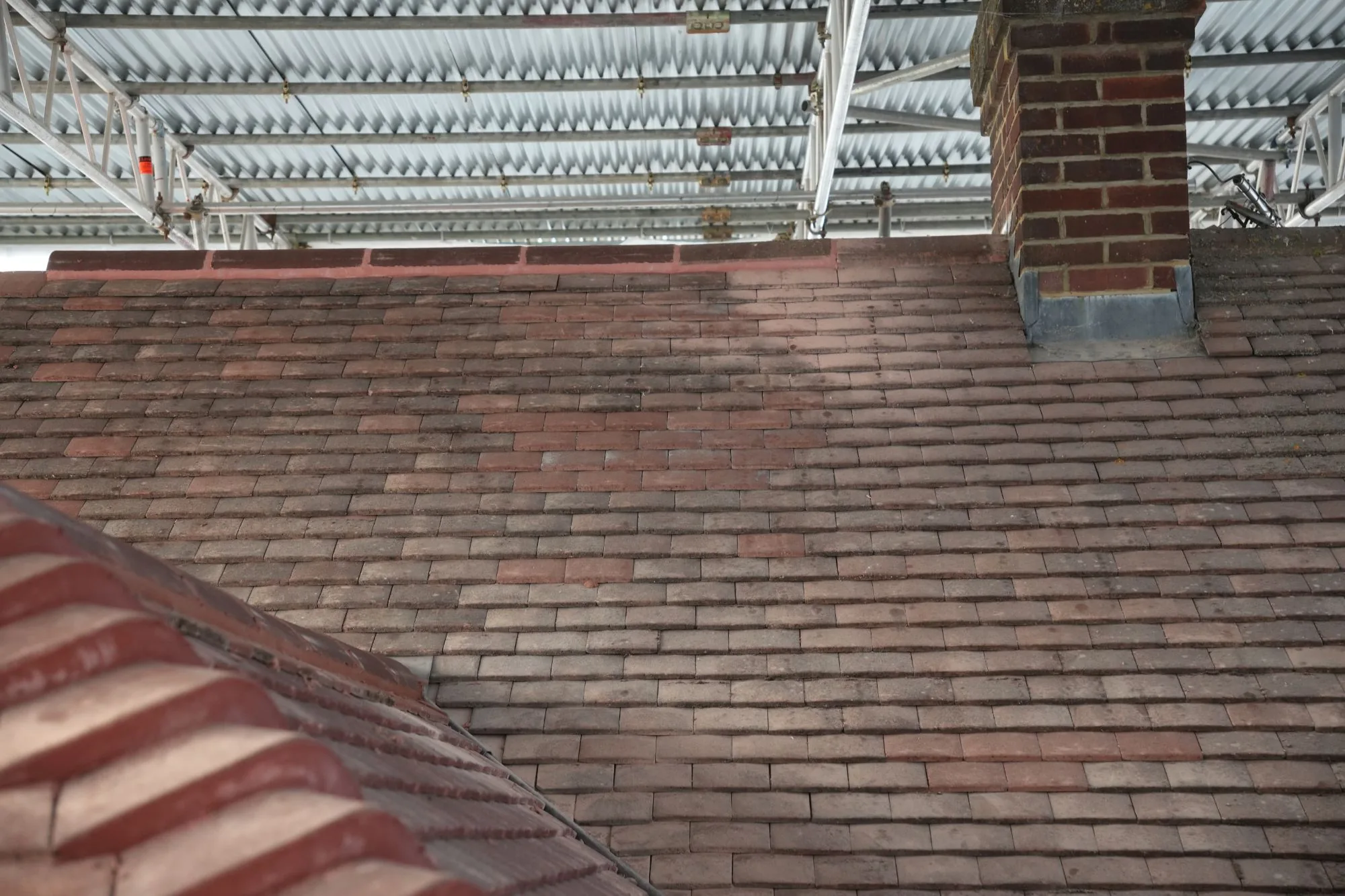 New plain tiles laid up to the chimney on the Brentwood roof, lead flashing dressed in, beneath the scaffold's temporary roof.