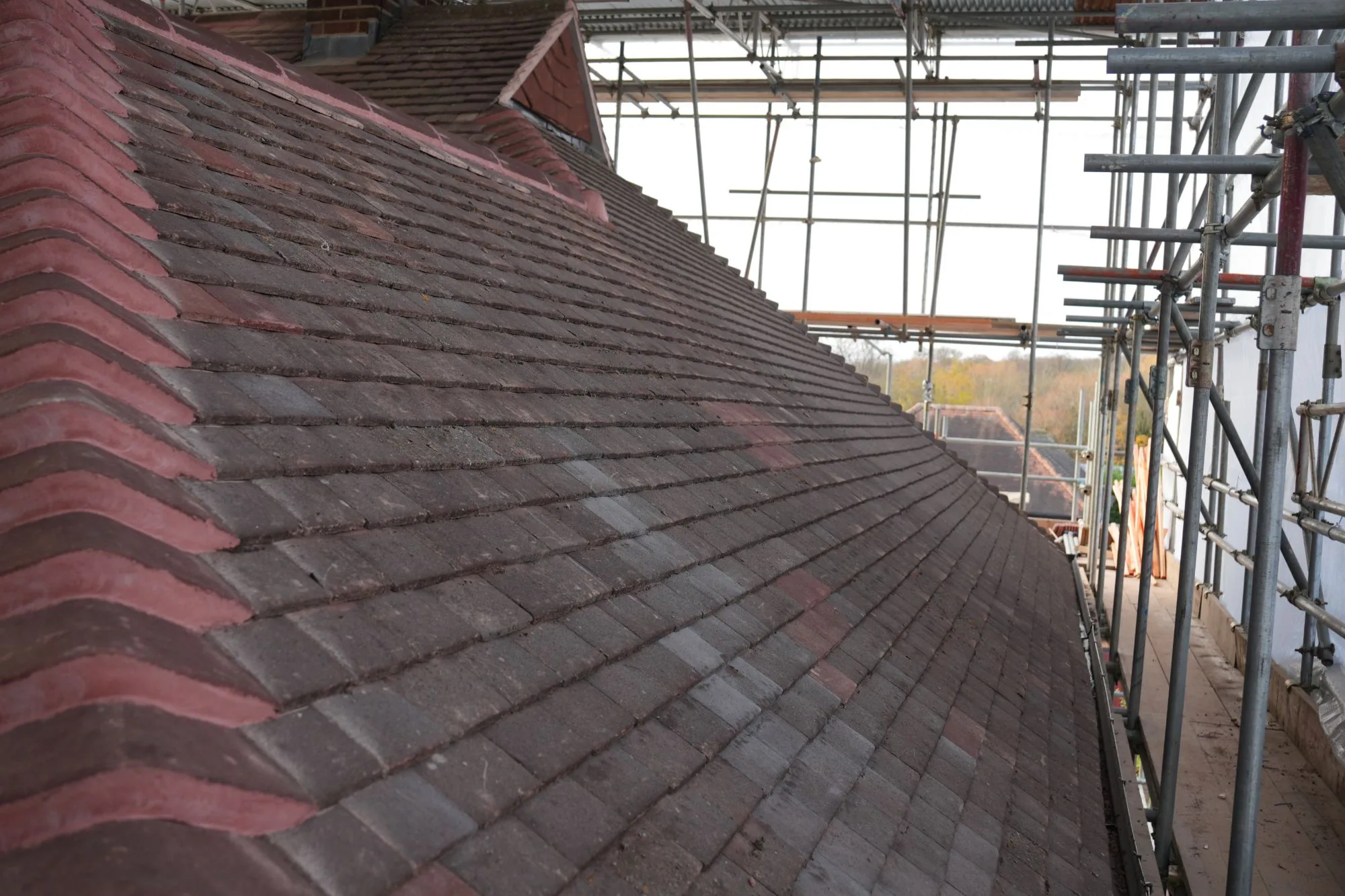 A completed run of new plain tiles on the redesigned Brentwood roof, seen along the scaffold walkway with neighbouring rooftops beyond.