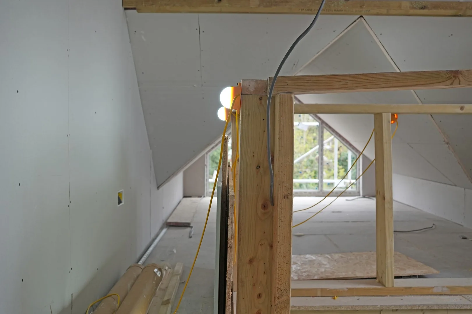 First fix timber framing in the Chigwell loft: new stud partitions under the plasterboarded roof slopes, with the glazed gable beyond.
