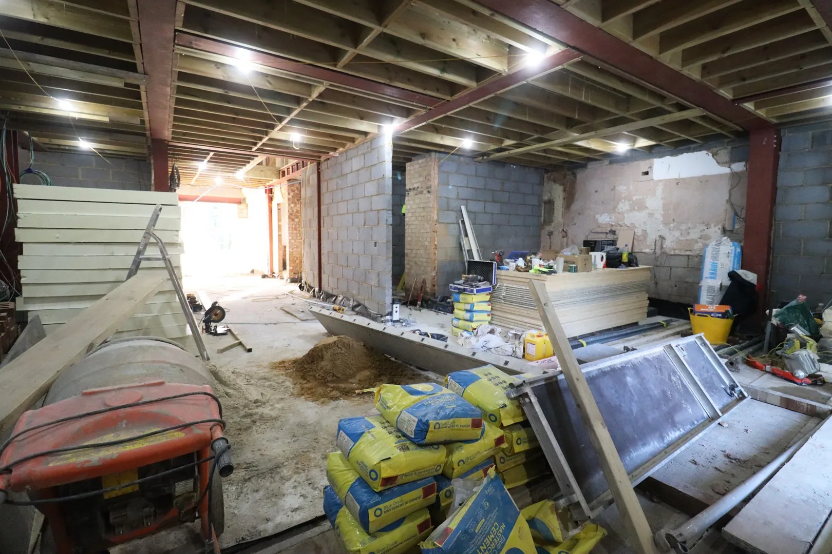 A second structural interior at Chigwell: steels and new timber joists over blockwork walls, with the mixer and materials of a working site.