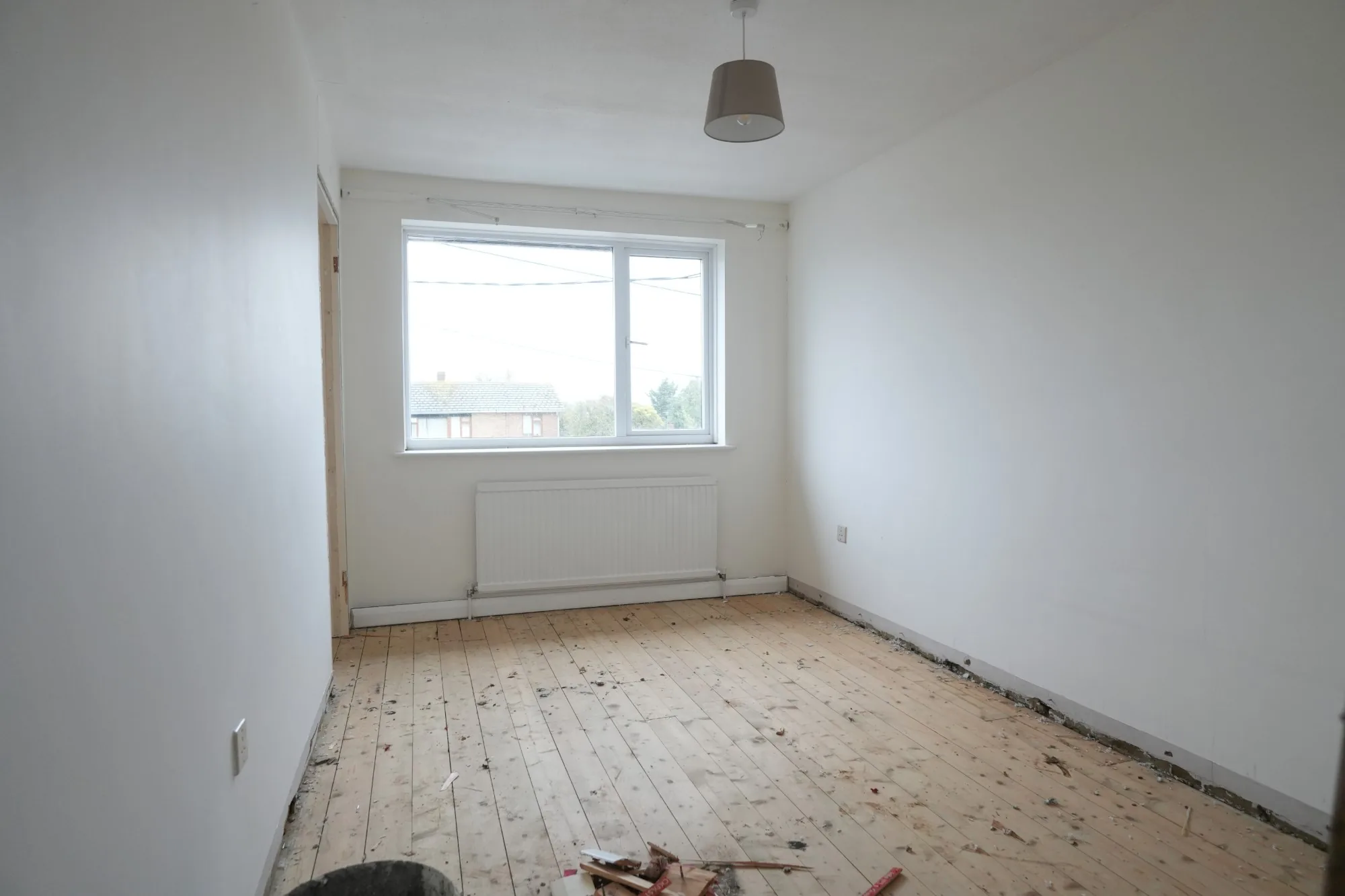 A plain, dated bedroom at Cold Norton as bought, bare boards and an old radiator under the window.