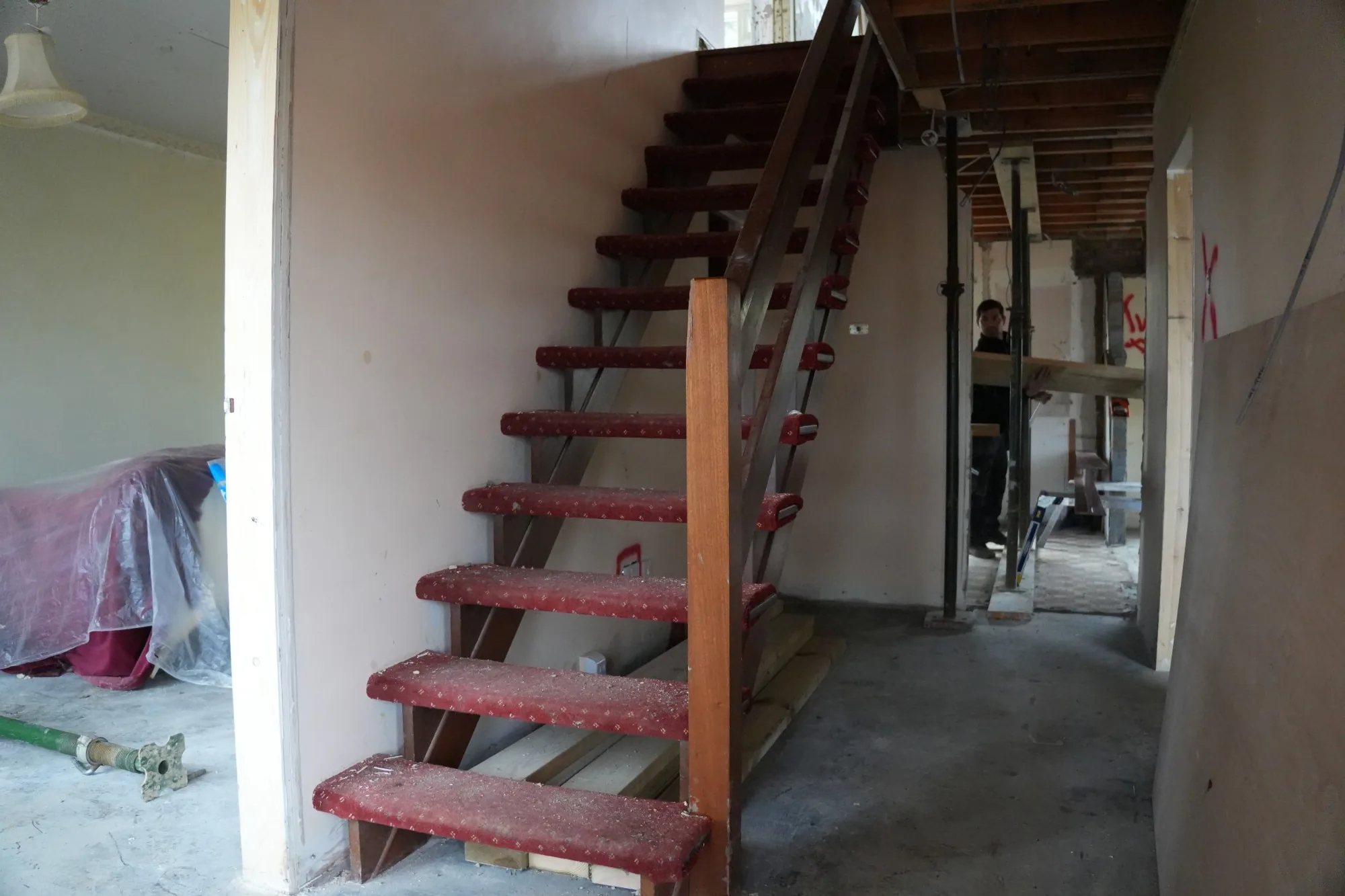 The dated hallway and red-carpeted staircase, the furniture sheeted over as the work started around it.