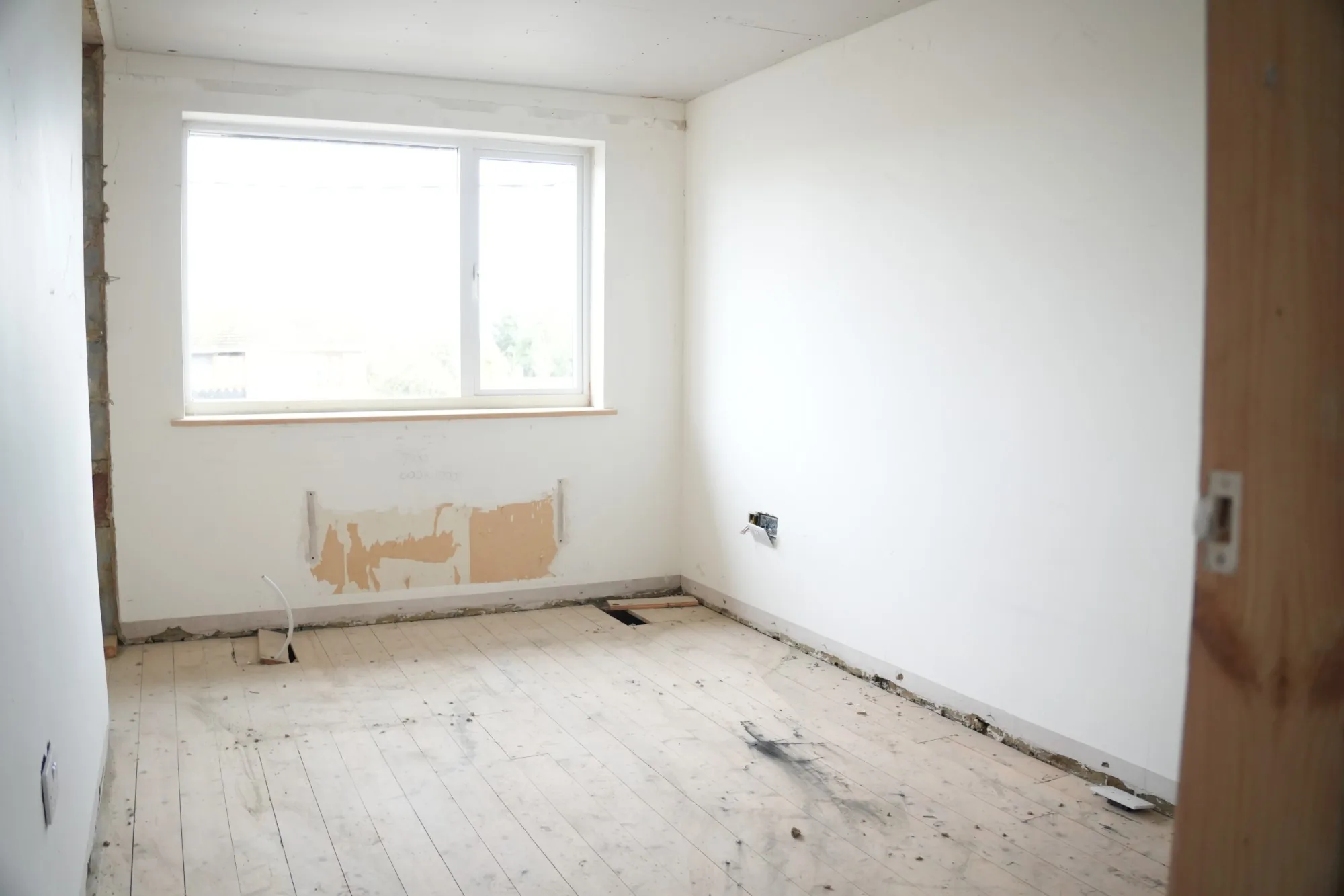 A dated bedroom stripped of its furnishings, radiator removed and sizing notes pencilled on the wall.