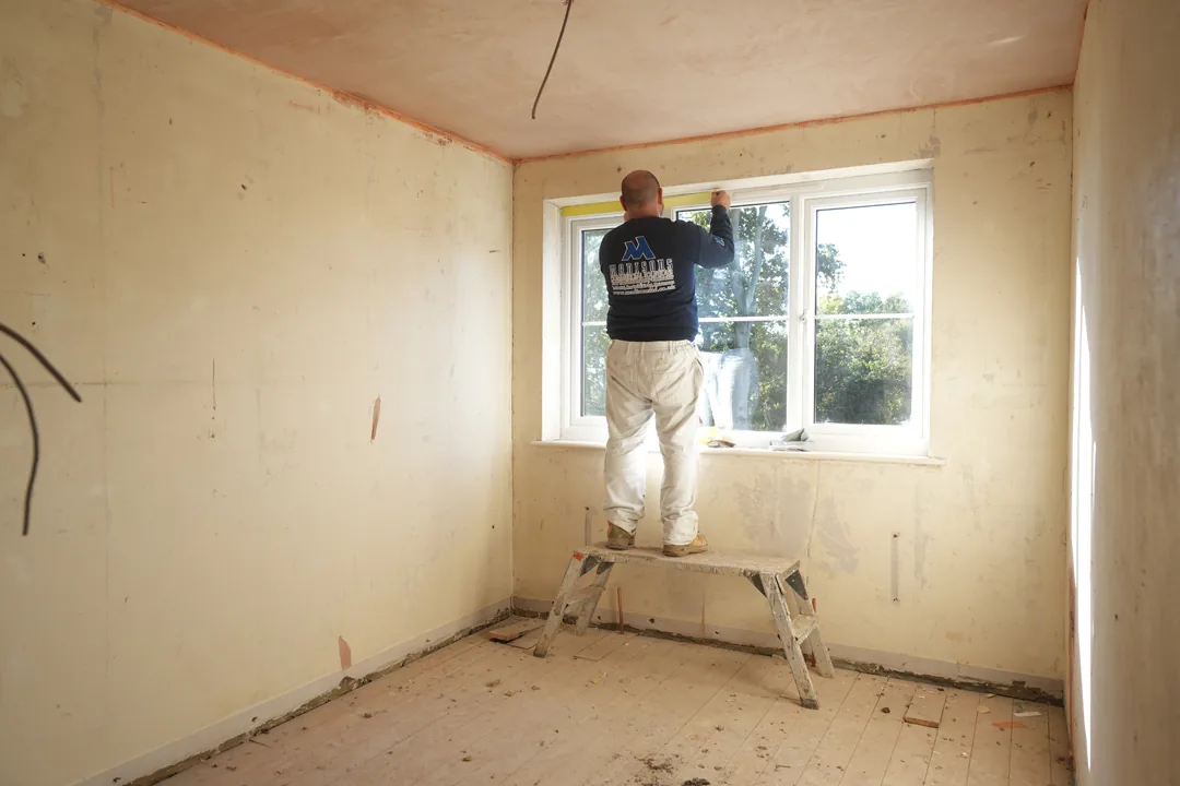 A Madisons operative in company uniform working at a window reveal beneath a freshly plastered ceiling.