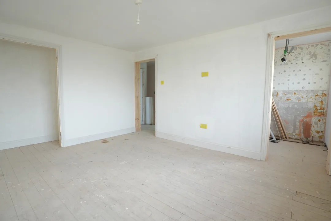 A freshly plastered and painted bedroom, with the last of the old wall surfaces still visible in the room beyond.