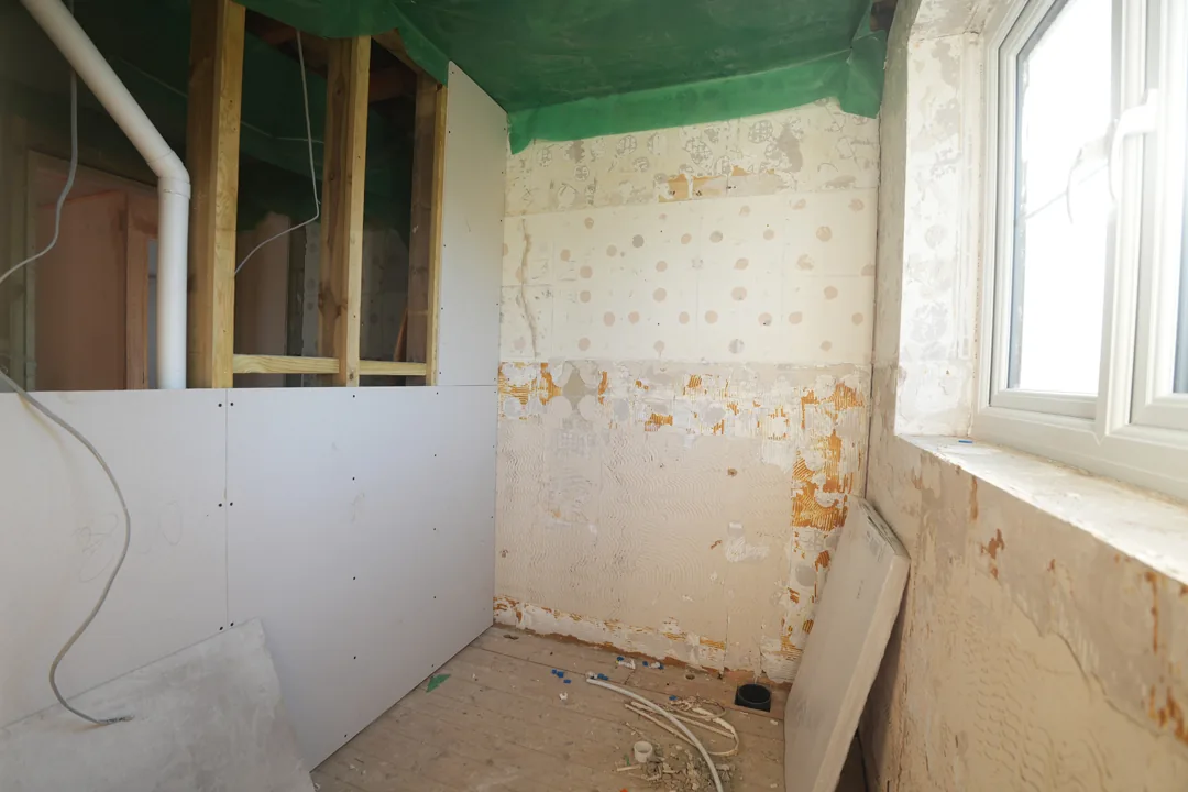 New stud partitions and plasterboard going in against the old tiled walls of a stripped bathroom.