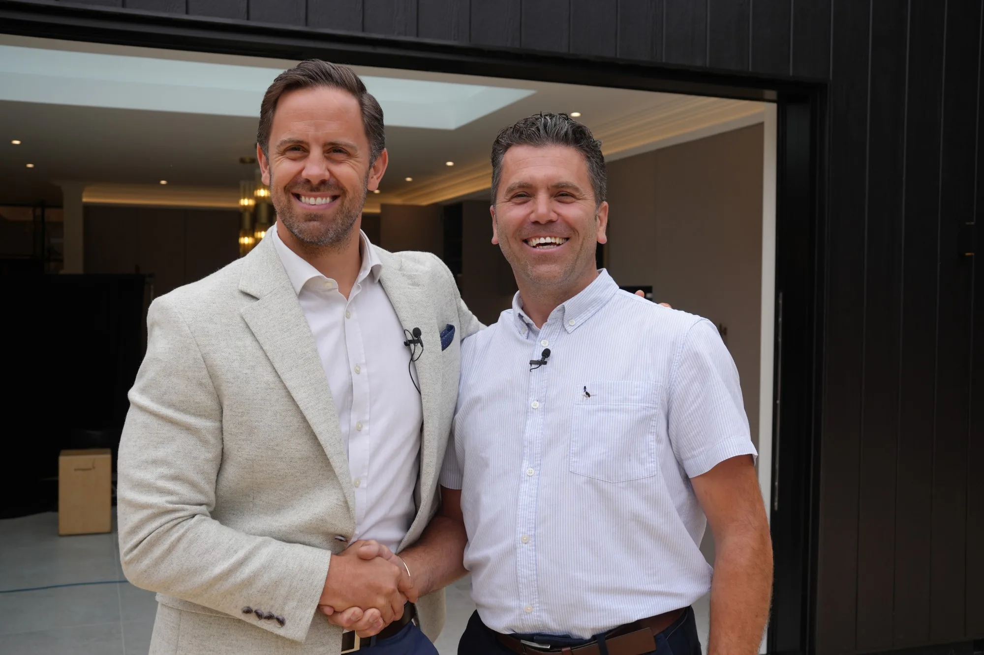 Craig Bellamy shaking hands with another man outside a completed project, dark timber cladding and open sliding doors behind them
