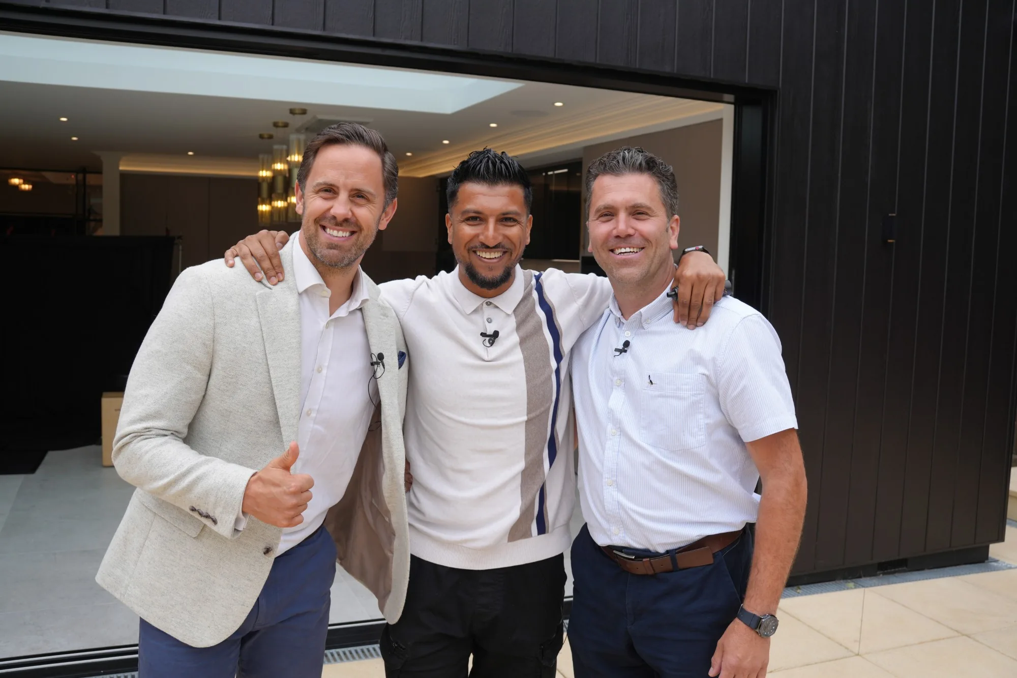 Craig Bellamy with two other men at the same completed project, all three smiling and wearing lapel microphones
