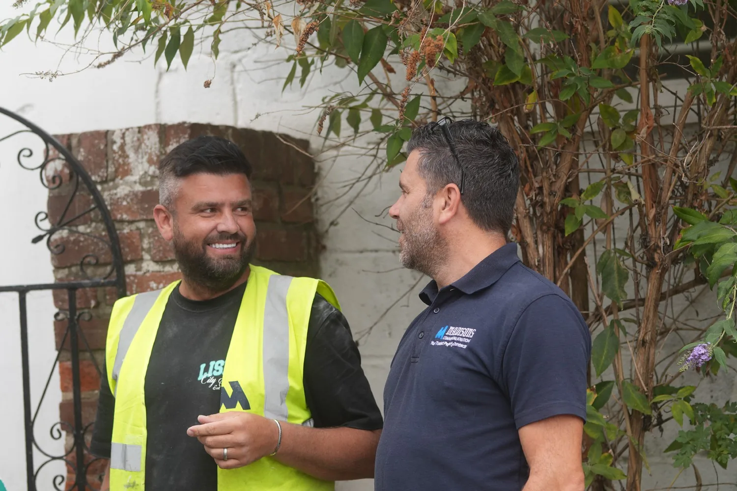 Two of the Madisons team talking by the garden gate on site at Heathcote Prep School, Danbury, one in a hi-vis vest and one in the company polo shirt.