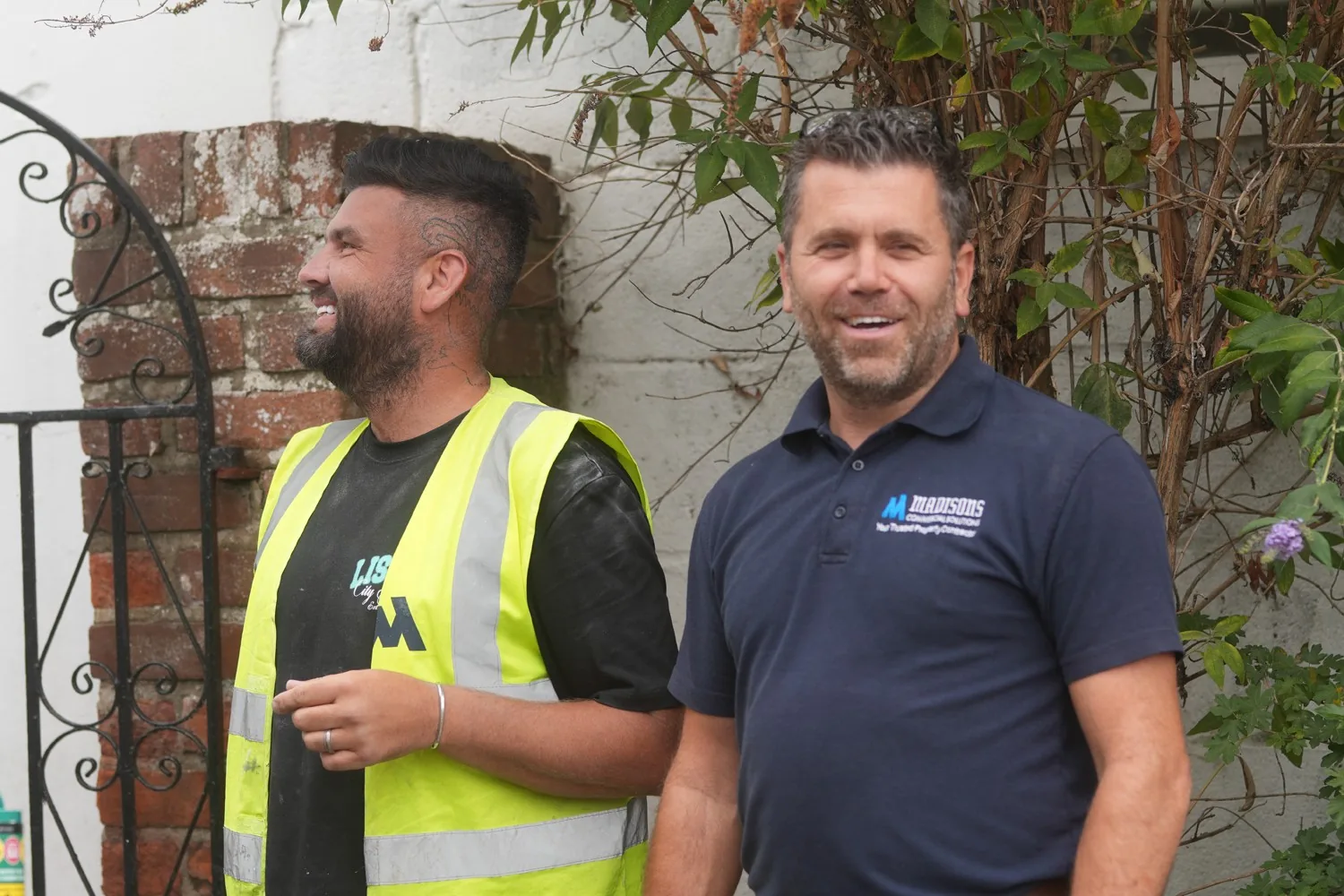 Two smiling Madisons team members on site at Heathcote Prep School, Danbury, one in a hi-vis vest and one in the company polo shirt.