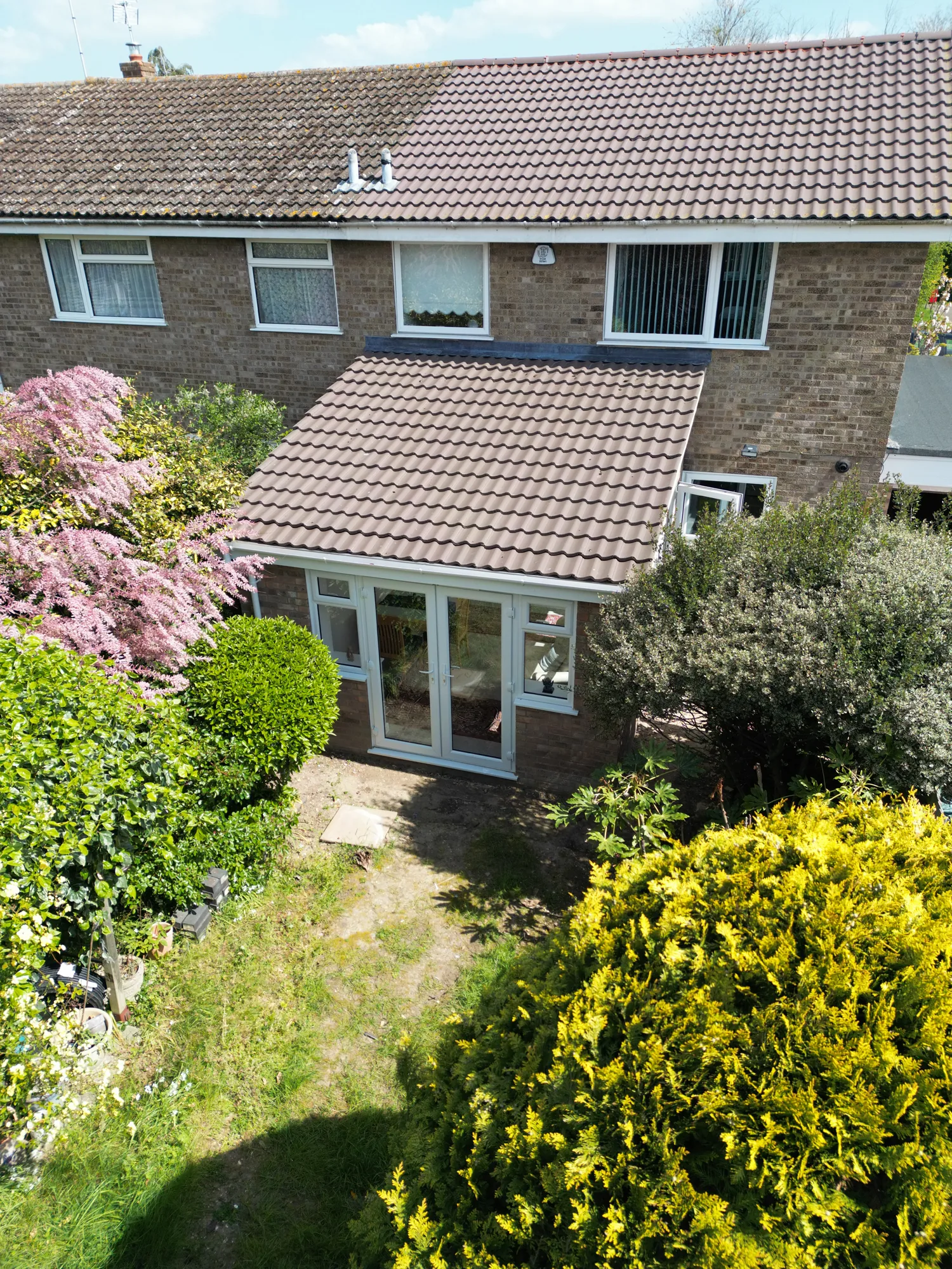 Drone view of the rear of the Witham house showing the single storey extension with its tiled roof, French doors and the garden.