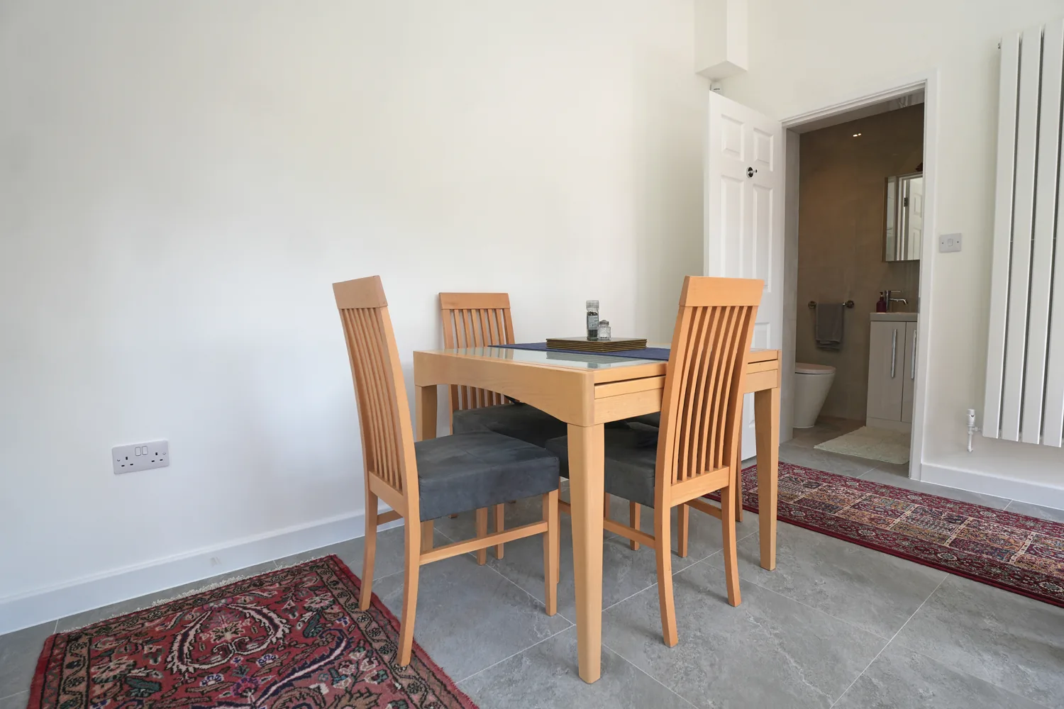 The dining table in the Witham extension beside a tall white column radiator, with the door open to the new shower room.
