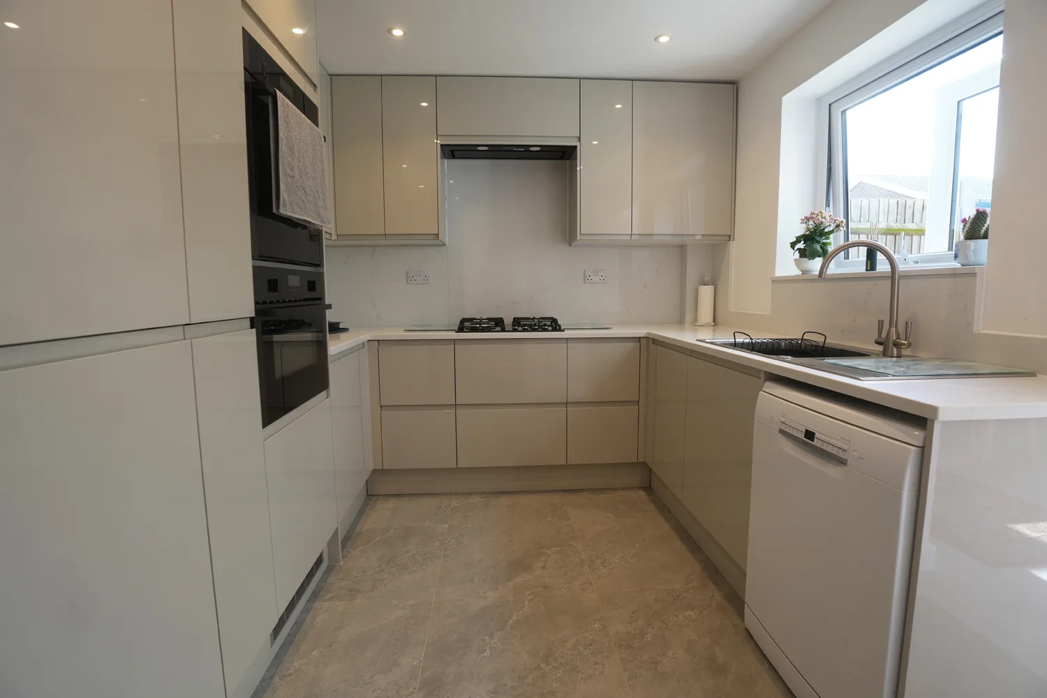 The galley style kitchen in the Witham house running to the window, with gas hob and extractor, tall units and a white dishwasher.
