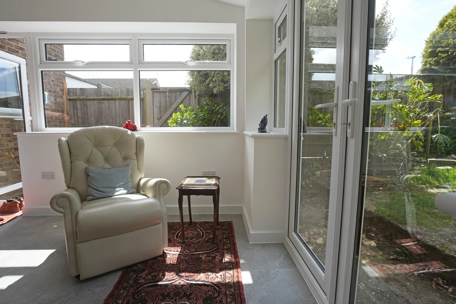 An armchair in the corner of the Witham extension beneath the side windows, with a French door open to the garden.