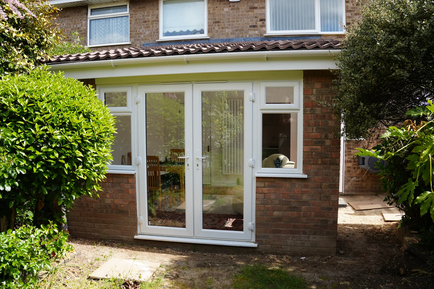 The rear of the finished Witham extension from the garden: brick walls, a tiled pitched roof, white French doors and side windows.