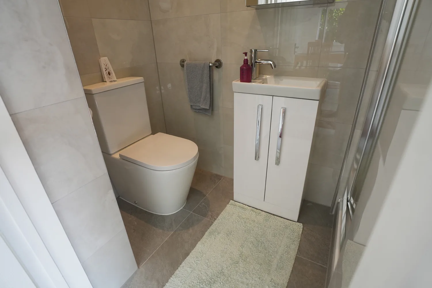 The compact shower room off the Witham extension, with large format wall tiles, a white vanity basin unit, toilet and towel ring.