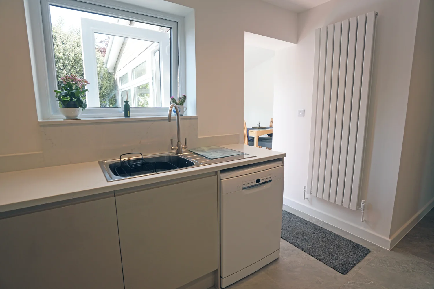 The sink run under the Witham kitchen window with a white dishwasher and tall radiator, the extension dining area visible beyond.