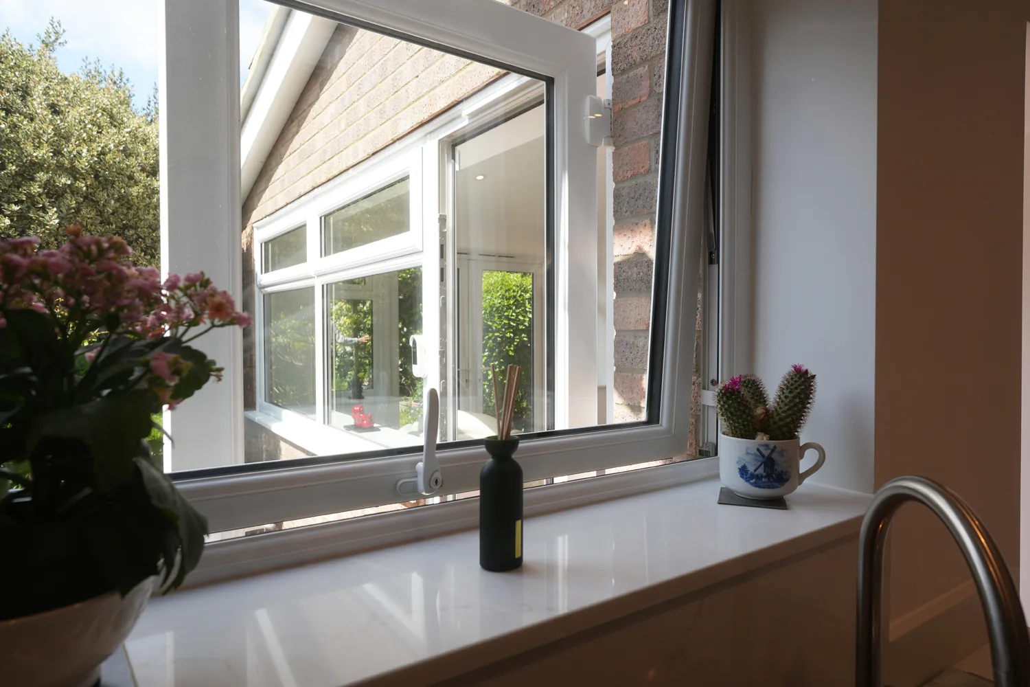 The stone window sill at the Witham kitchen sink, with plants, looking out to the windows of the new extension.