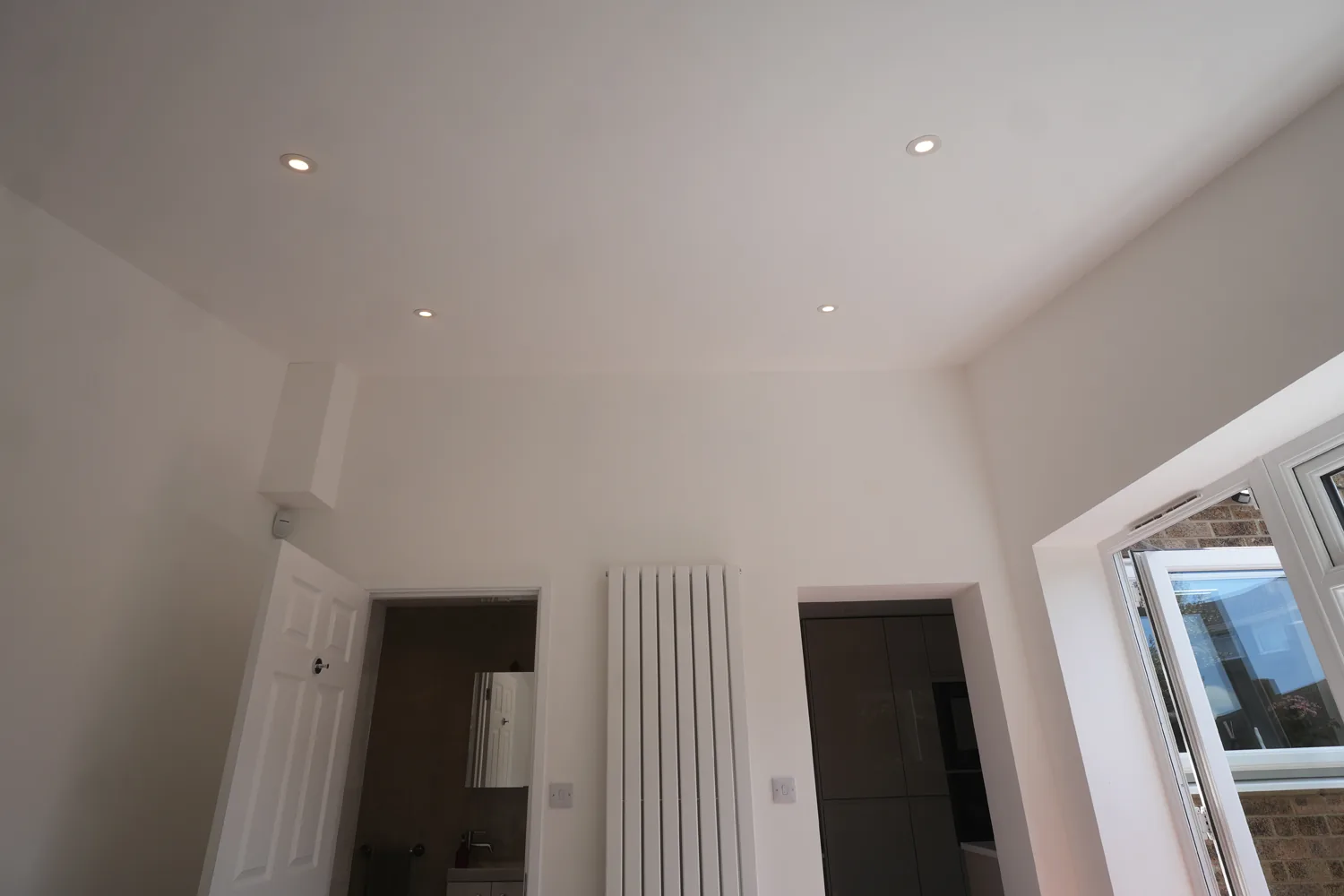 Looking back from the Witham extension towards the house: the vaulted ceiling with downlights and a tall radiator between the doors to the shower room and the kitchen.